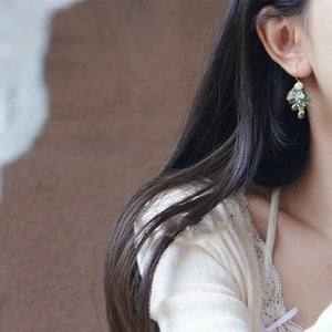 Close-up of a model wearing one green glass grape cluster dangle earring with a pearl bead