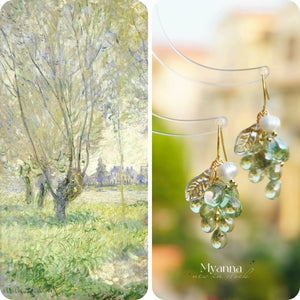 Split promotional graphic: impressionist painting of willow trees by a river on the left, and green glass grape cluster dangle earrings with pearl beads on a clear acrylic stand on the right, with Myanna new in stock text