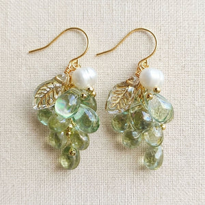 Pair of purple and green Czech glass grape earrings hanging against a neutral linen background