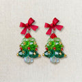 Close-up of emerald green acrylic Christmas tree earrings featuring hand-set red pearls and crystal snowflakes