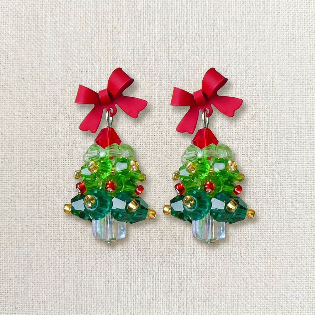 Close-up of emerald green acrylic Christmas tree earrings featuring hand-set red pearls and crystal snowflakes