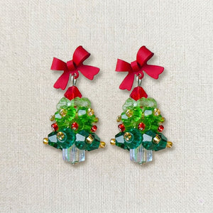 Close-up of emerald green acrylic Christmas tree earrings featuring hand-set red pearls and crystal snowflakes