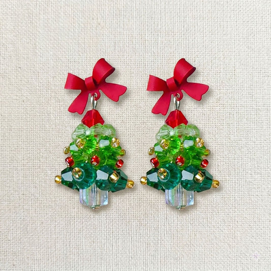 Close-up of emerald green acrylic Christmas tree earrings featuring hand-set red pearls and crystal snowflakes