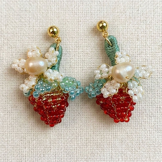 Close-up of hand-woven strawberry flower earrings showing intricate red cotton stitching and white flower petals