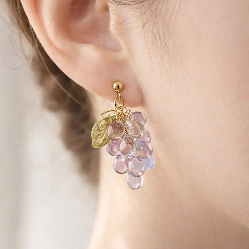 Woman wearing handmade Czech glass earrings with light purple translucent grape beads and green leaf accents, nature‑inspired bohemian jewelry for women
