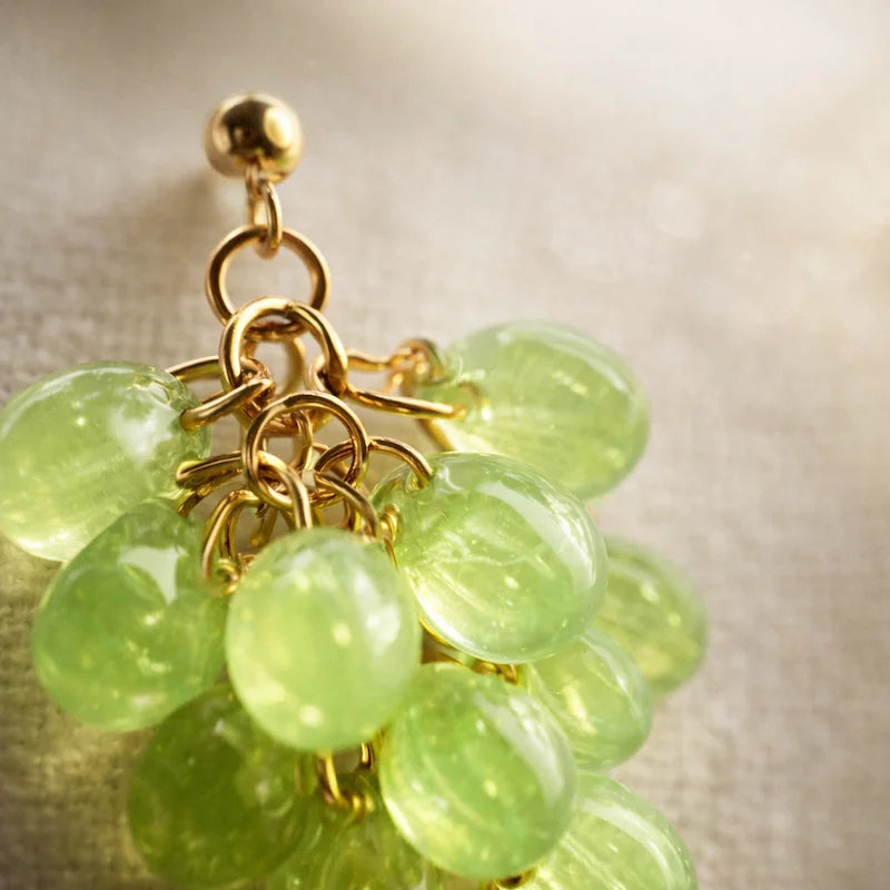Close‑up of handmade Czech glass earrings with light green translucent beads and gold detailing, elegant artisan jewelry for women