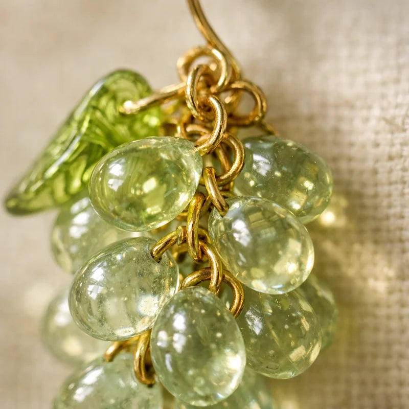 Close‑up of handmade Czech glass earrings with light green translucent grape beads and green leaf accents, nature‑inspired bohemian jewelry for women