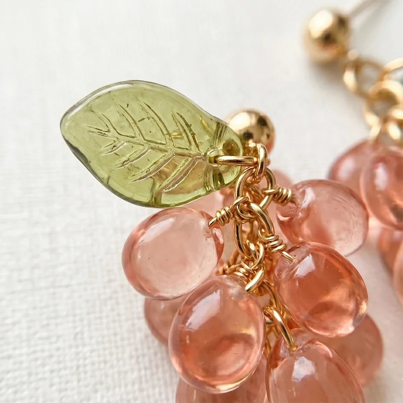 Close‑up of handmade Czech glass earrings with translucent pink grape beads and green leaf accents, nature‑inspired bohemian jewelry for women