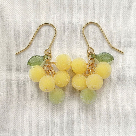 Flatlay of frosted grape earrings on unbleached linen fabric showing artisan texture