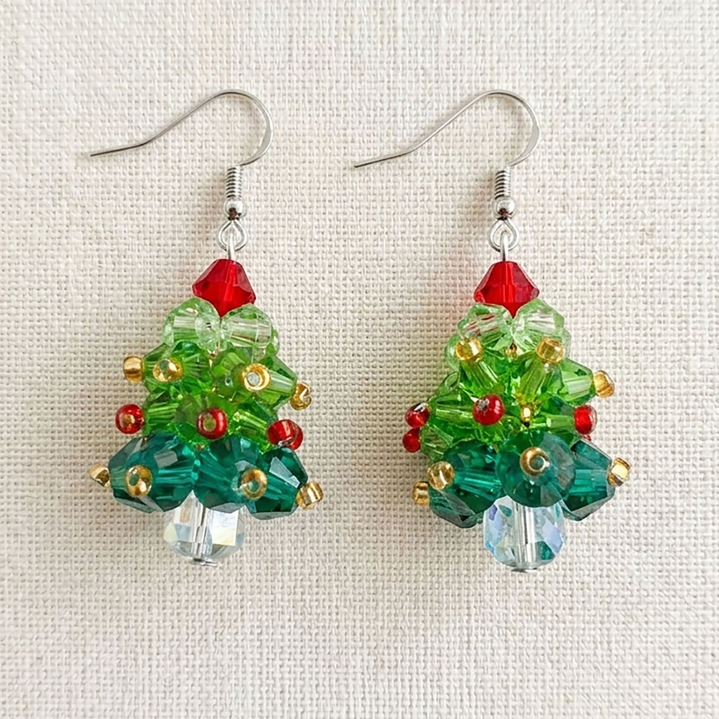 Flatlay of handcrafted acrylic holiday earrings on a natural linen background with seasonal decorations