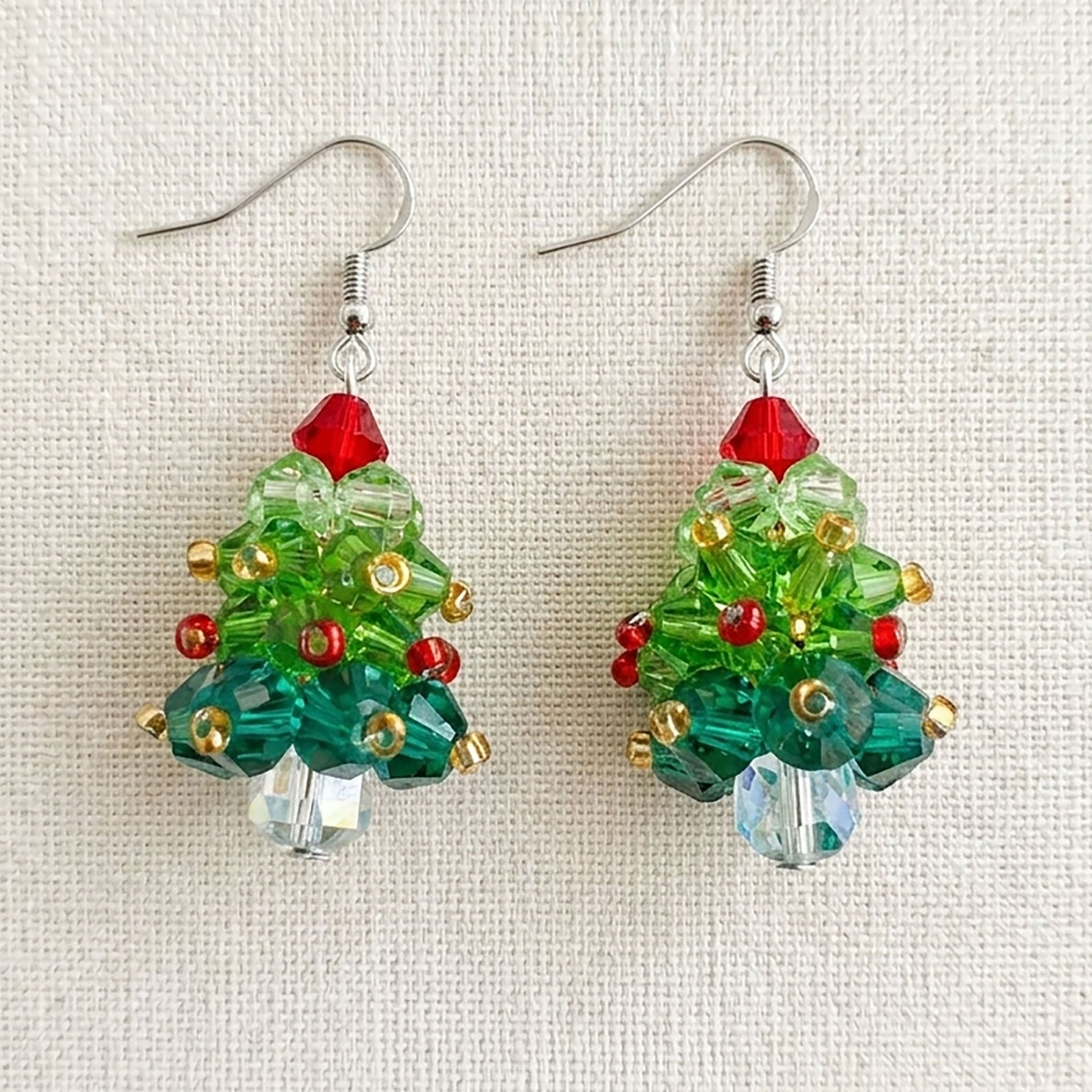 Flatlay of handcrafted acrylic holiday earrings on a natural linen background with seasonal decorations
