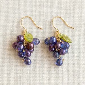 Flatlay of purple grape cluster earrings on unbleached linen fabric with antique bronze hooks