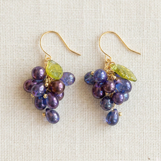 Flatlay of purple grape cluster earrings on unbleached linen fabric with antique bronze hooks