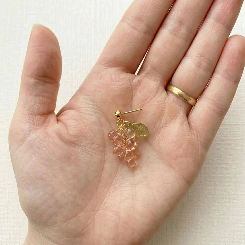 Hand‑held view of handmade Czech glass earrings with translucent pink grape beads and gold leaf detailing, delicate nature‑inspired jewelry for women