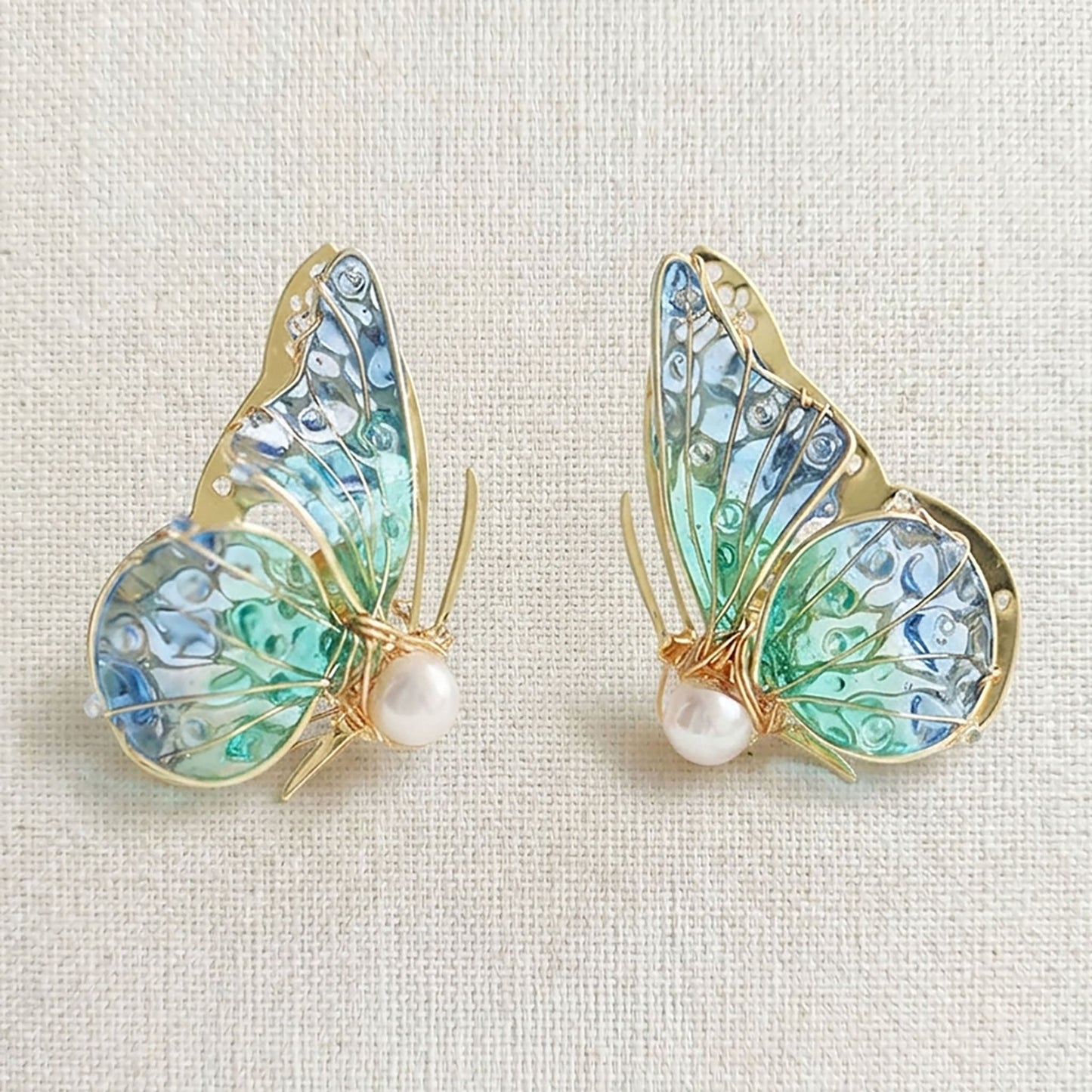 Handmade butterfly earrings with blue-green translucent wings, gold detailing and pearl accent, elegant Western-style jewelry for women in the US and Europe
