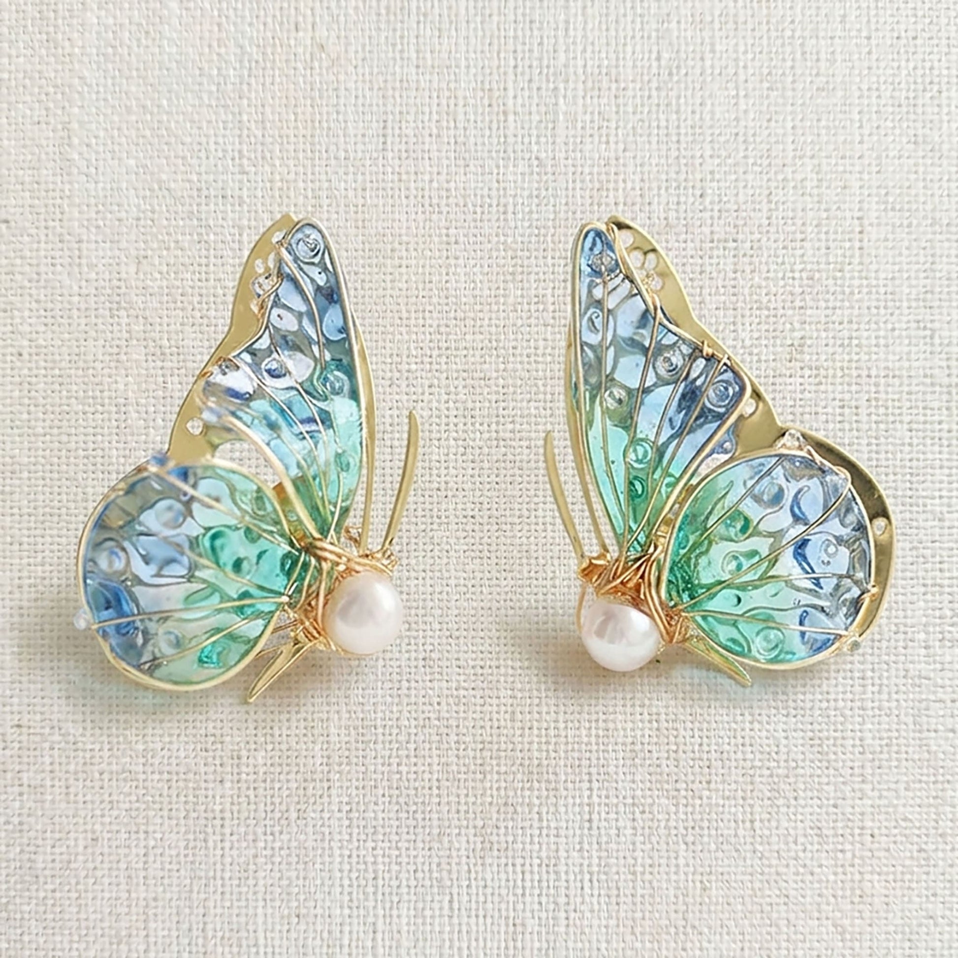 Handmade butterfly earrings with blue-green translucent wings, gold detailing and pearl accent, elegant Western-style jewelry for women in the US and Europe