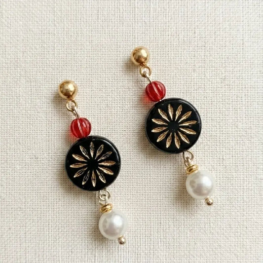 “Handmade earrings with red bead, black gold floral medallion and white pearl drop on fabric background, elegant jewelry for women