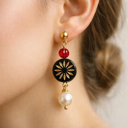 Handmade earrings with red bead, black gold floral medallion and white pearl drop worn by model, elegant jewelry for women