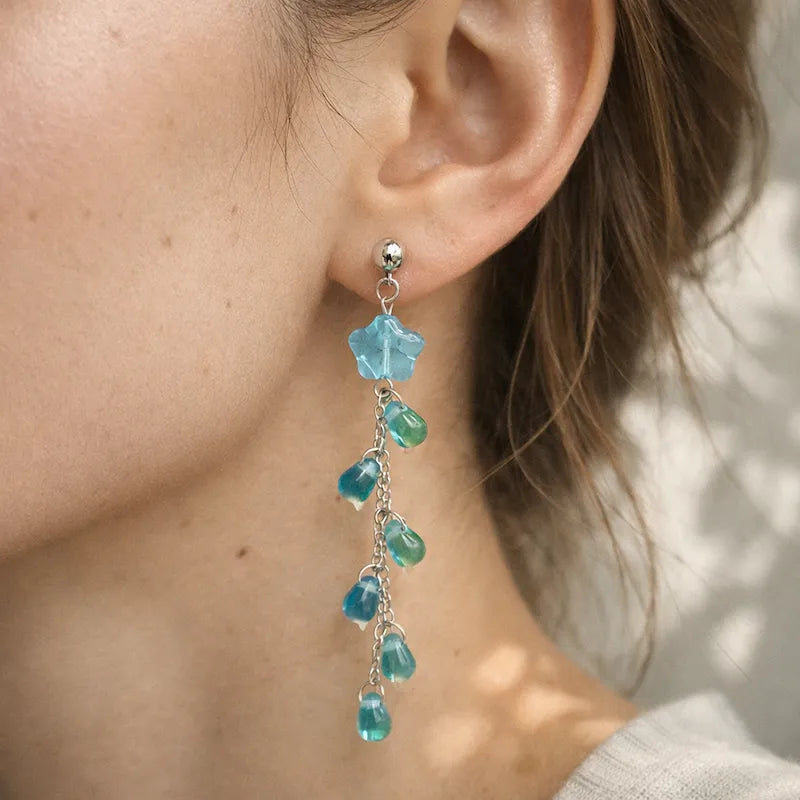 Handmade floral drop earring with blue translucent flower bead, green and blue teardrop accents on silver chain worn by model, elegant Western‑style jewelry for women in the US and Europe