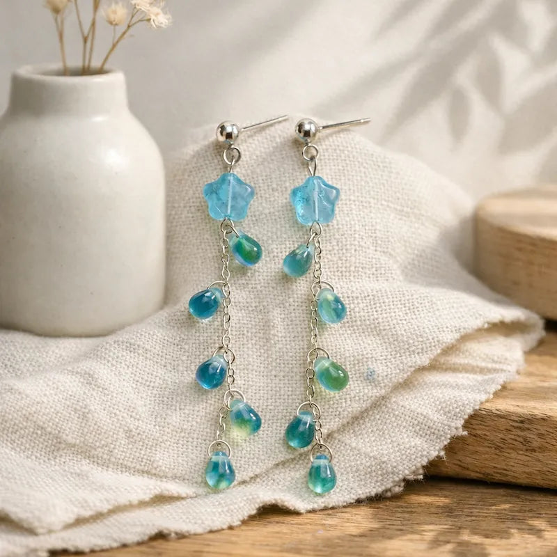 Handmade floral drop earrings with blue translucent flower bead, green and blue teardrop accents on silver chain, elegant Western‑style jewelry for women in the US and Europe