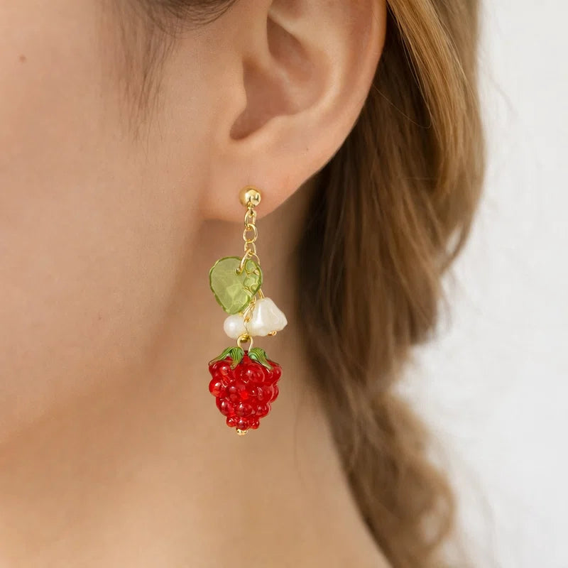 Handmade fruit-inspired earrings with red strawberry bead, green leaf charm and white flower detail worn by model, elegant Western-style jewelry for women in the US and Europe