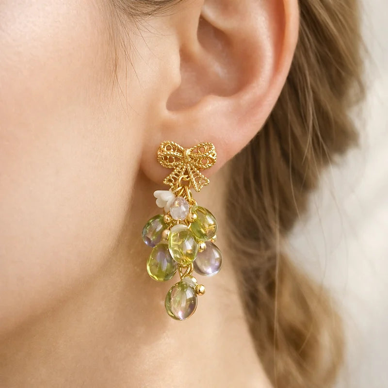 Handmade grape‑inspired earring with gold bow, green and purple translucent beads and pearl accents worn by model, elegant Western‑style jewelry for women in the US and Europe