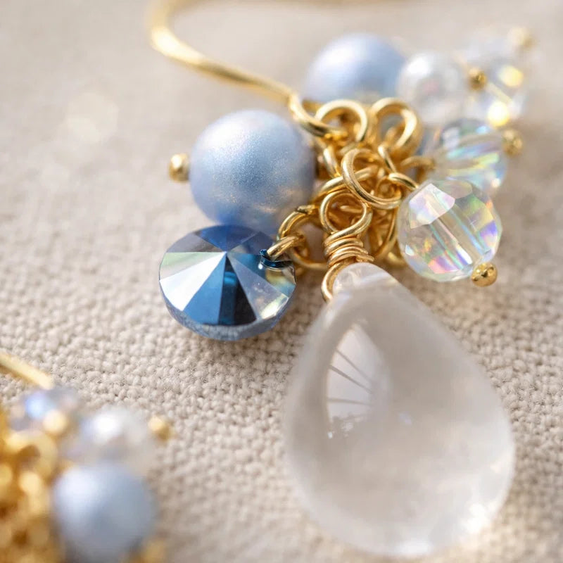 Handmade jewelry detail with clear teardrop crystal, blue faceted bead and iridescent accents on gold setting, elegant Western‑style accessory for women in the US and Europe