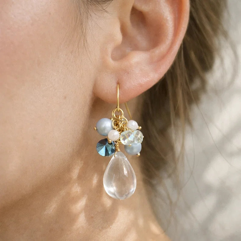 Handmade teardrop crystal earring with clear gemstone, blue and white bead cluster and gold detailing worn by model, elegant Western‑style jewelry for women in the US and Europe