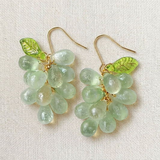 Pair of handmade purple glass grape drop earrings with gold hooks on a linen background