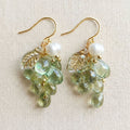 Pair of purple and green Czech glass grape earrings hanging against a neutral linen background