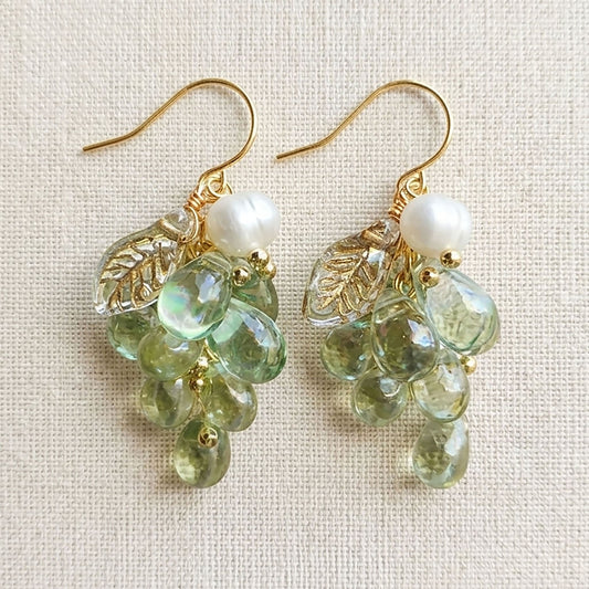 Pair of purple and green Czech glass grape earrings hanging against a neutral linen background