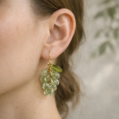 Woman wearing handmade Czech glass earrings with light green translucent grape beads and green leaf accents, nature‑inspired bohemian jewelry for women