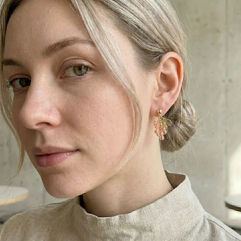 Woman wearing handmade Czech glass earrings with translucent pink grape beads and gold leaf detailing, elegant nature‑inspired jewelry for women